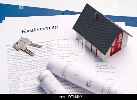 Model house, house keys and blueprints on a purchase contract for a property. Stock Photo