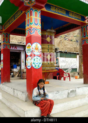 A young girl sits in front of the prayer drum of Hemis Monastery,Ladakh Stock Photo