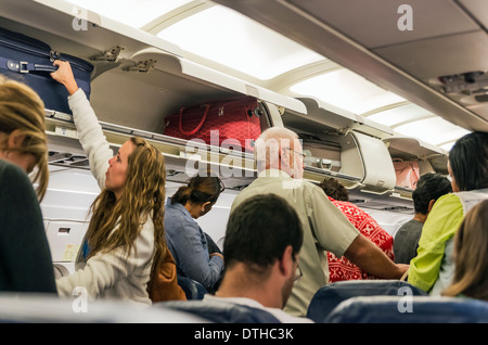 Airline travelers retieve their carry-on luggage from overhead compartments. Stock Photo