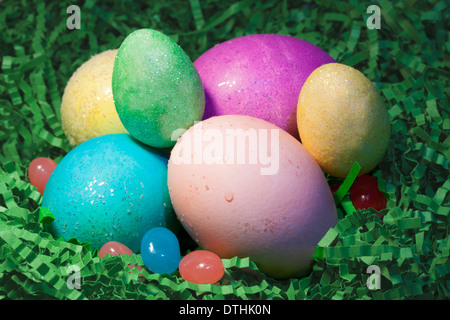 Colored Easter eggs in Easter grass with jelly beans. Stock Photo