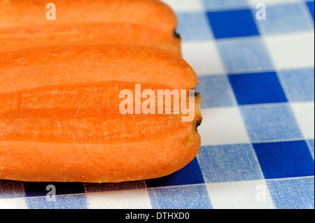A fresh carrot cut into 2 pieces on a blue gingham background Stock Photo