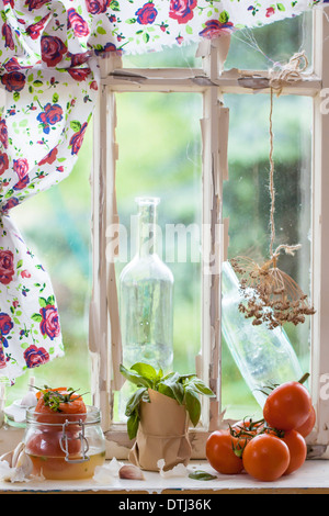 Fresh and canned tomatoes, vintage bottles and basil on old windowsill in natural light Stock Photo