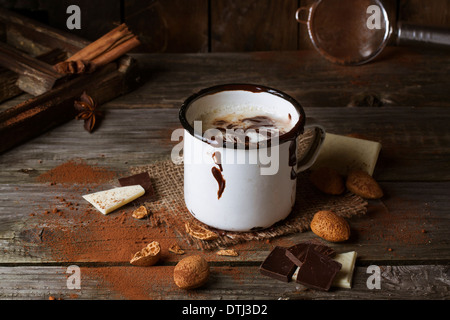 Vintage mug with hot chocolate served with chunks of white and dark chocolate and almonds on old wooden table Stock Photo