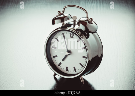 metallic Alarm clock on dark bedside table Stock Photo