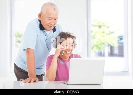 Senior couple using a laptop and a cell phone at home Stock Photo