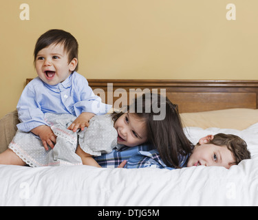 Three children in a family lying playing on a large bed  Pennsylvania USA Stock Photo