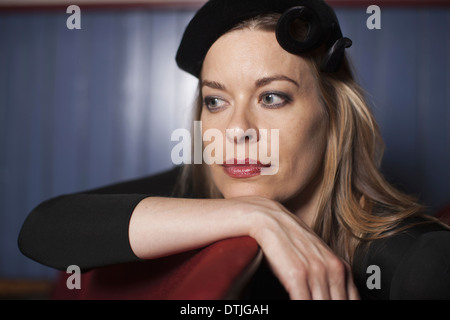 A woman in a theatre wearing an evening hat and black top Resting her chin on her hand looking away in an elegant pose Stock Photo