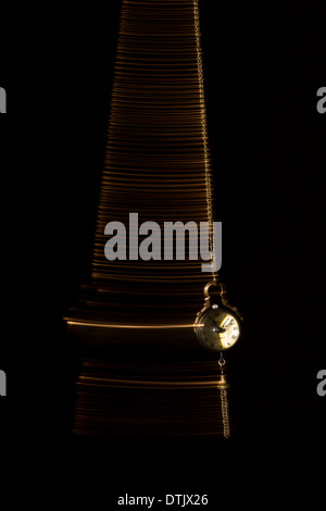 Gold pocket watch swinging side to side to indicate the passing of time, on a black background. Stock Photo