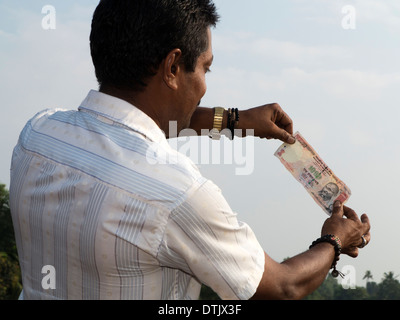India, Kerala, money, Indian man holding up 1000 rupee note to light to check watermark Stock Photo