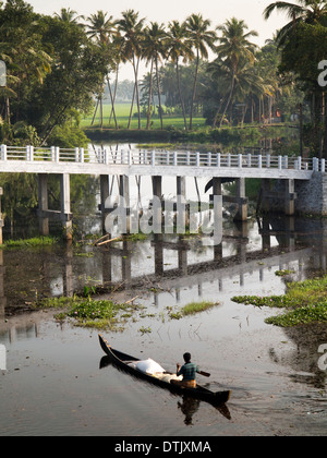 India, Kerala, backwaters, man in traditional wooden canoe passing under modern concrete bridge Stock Photo