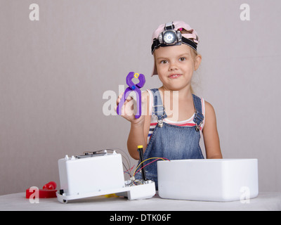 Girl playing in the repairer and repairs toy microwave. A girl Holds the pliers in which clamped nut and looks in a frame Stock Photo
