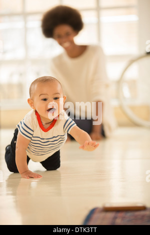 Mother watching baby boy crawl on floor Stock Photo