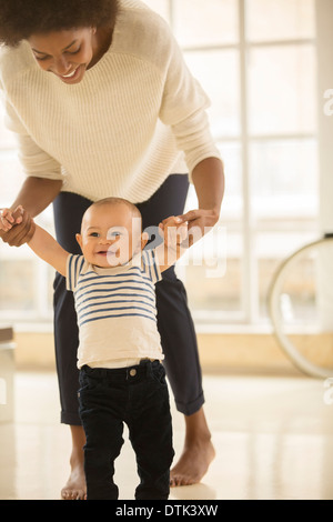 Mother helping baby boy walk on floor Stock Photo