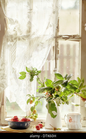 Bouquet from branches of apple and plum trees and a bowl of strawberries on an old window sill Stock Photo