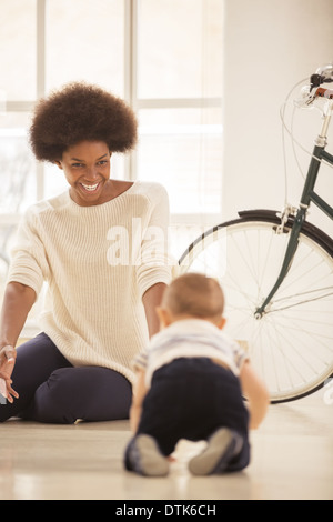 Mother watching baby boy crawl in living room Stock Photo