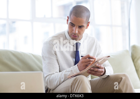 Businessman making notes from laptop on sofa Stock Photo
