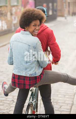Couple riding bicycle together on city street Stock Photo
