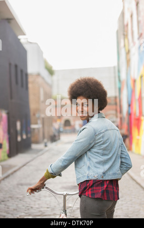 Woman pushing bicycle on city street Stock Photo