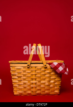 A brown, wicker picnic basket with red gingham tablecloth on a red background with copy space Stock Photo