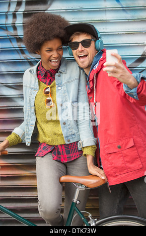 Couple taking self-portrait with cell phone against graffiti wall Stock Photo