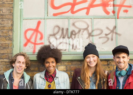 Friends smiling together in front of graffiti window Stock Photo