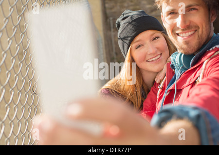 Couple taking self-portrait with camera phone next to chain link fence Stock Photo