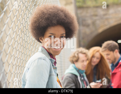 Woman smiling by chain link fence with friends in background Stock Photo