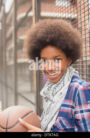 Woman holding basketball against fence Stock Photo