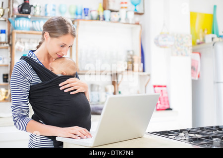 Mother with baby boy using laptop in kitchen Stock Photo