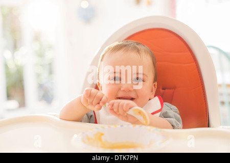 Baby boy eating in high chair Stock Photo