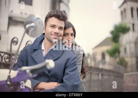 Couple sitting on scooter on city street Stock Photo