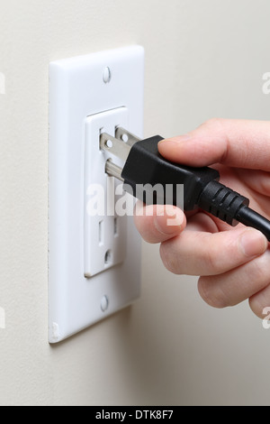 Closeup of a woman's hand inserting an electrical plug into a wall socket Stock Photo