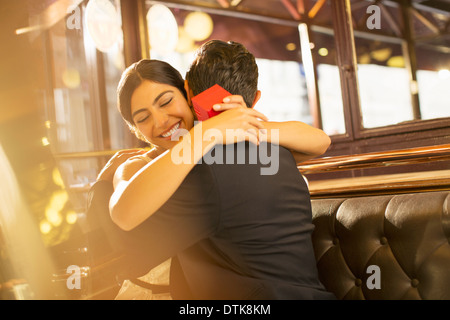 Woman with jewelry box hugging man in restaurant Stock Photo