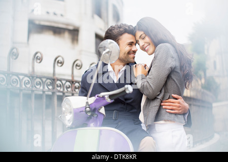 Couple hugging on scooter on city street Stock Photo