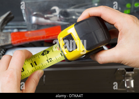 Horizontal photo of female hands pulling used tape measure out with old toolbox in background Stock Photo