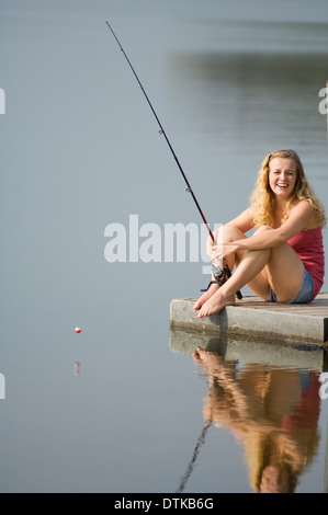 A young woman sitting on a dock fishing Stock Photo