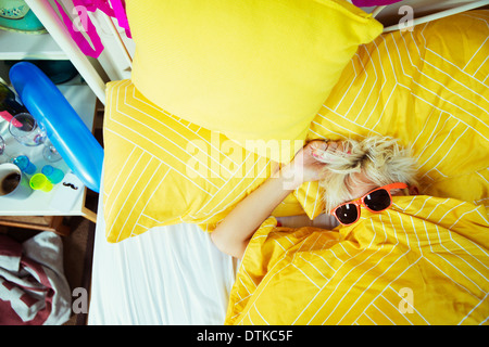 Woman wearing sunglasses in bed after party
