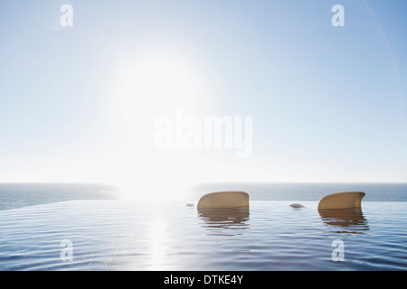 Lawn chairs in infinity pool overlooking ocean Stock Photo