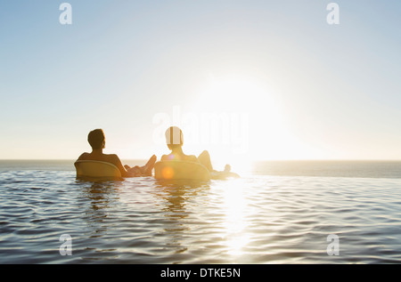 Couple in lounge chairs in infinity pool overlooking ocean Stock Photo
