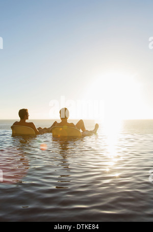 Couple in lawn chairs in infinity pool overlooking ocean Stock Photo