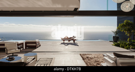 Woman sunbathing on lounge chair at poolside overlooking ocean Stock Photo