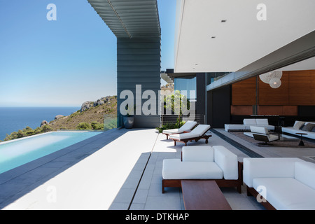 Lounge chairs and infinity pool on modern patio overlooking ocean Stock Photo