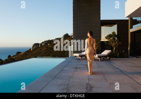 Woman in dress walking along infinity pool overlooking ocean Stock Photo