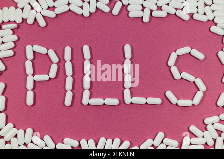 White pills on a red/pinks background spelling "PILLS". Stock Photo