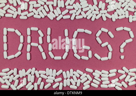 White pills on a red/pink background spelling "DRUGS?". Stock Photo