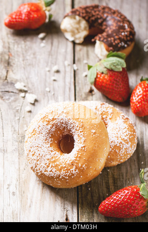 Sugar and chocolate donuts and fresh strawberries served on wooden table. See series Stock Photo