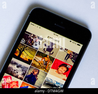 An iPhone 5S on a white  background, showing the Explore page of the Instagram app, which shows some of the most popular photos. Stock Photo