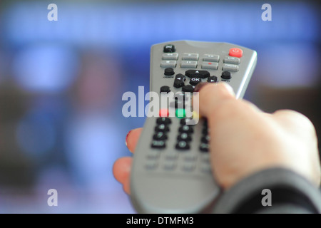 Woman holds remote control whilst watching television at home Stock Photo