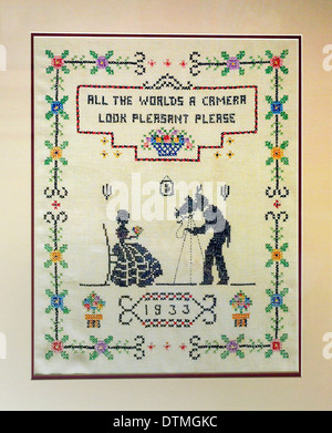A clever verse highlights this 1933 needlepoint sampler that shows a photographer with an old-fashioned camera taking a formal portrait of a woman. Stock Photo