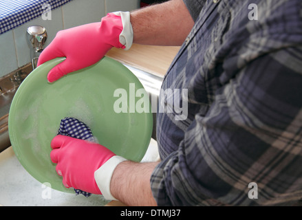 Man washing up pots/plate wearing pink rubber gloves at a kitchen sink at home, England, UK Stock Photo